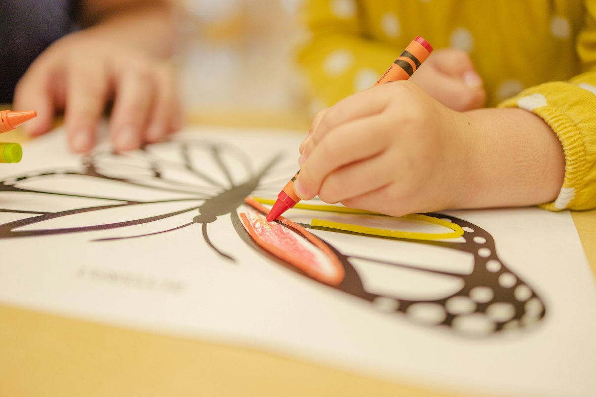 Le mani di un bambino che colora un disegno con i pastelli