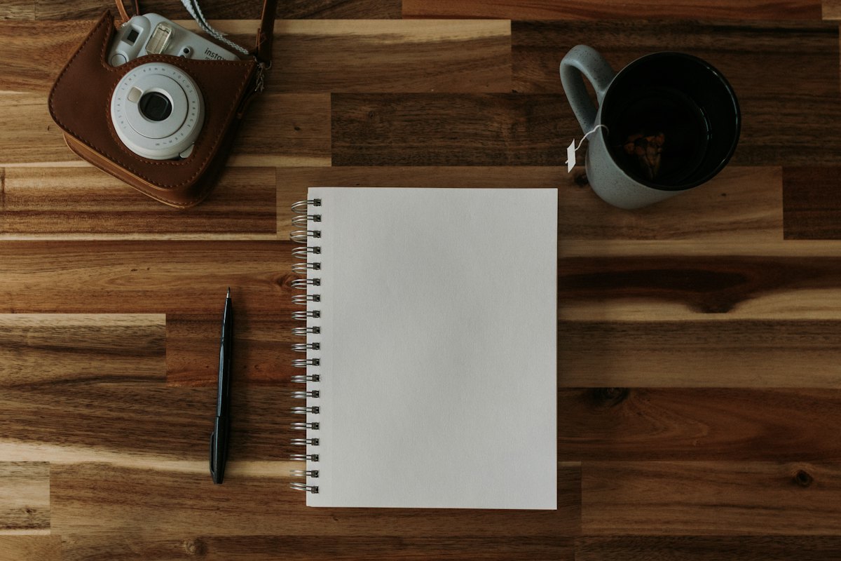 Un quaderno aperto, una penna e una tazza su un tavolo di legno